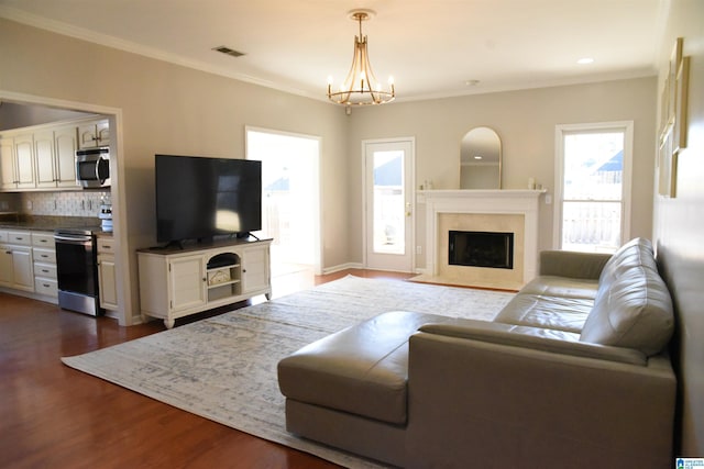 living room with a premium fireplace, dark hardwood / wood-style flooring, crown molding, and a notable chandelier