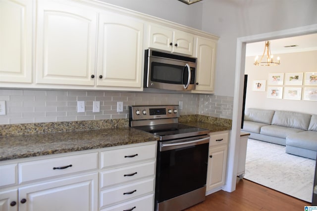 kitchen with dark wood-type flooring, an inviting chandelier, dark stone countertops, appliances with stainless steel finishes, and tasteful backsplash