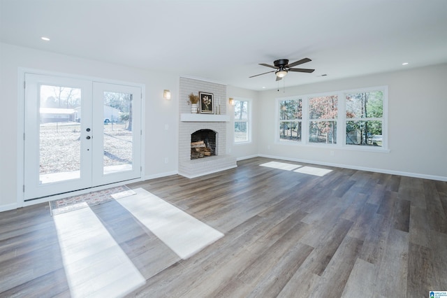 unfurnished living room with ceiling fan, french doors, wood-type flooring, and a brick fireplace