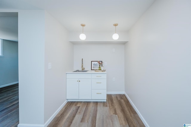 bar featuring white cabinets, decorative light fixtures, light wood-type flooring, and sink