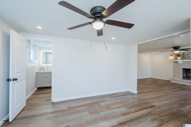 unfurnished living room featuring ceiling fan, sink, light hardwood / wood-style flooring, and a brick fireplace