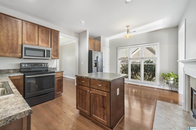 kitchen with light wood-type flooring, stainless steel appliances, pendant lighting, a fireplace, and a kitchen island