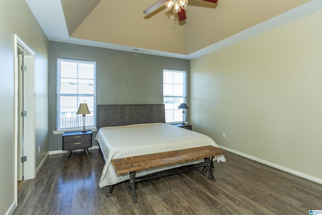 bedroom with multiple windows, a tray ceiling, ceiling fan, and dark wood-type flooring