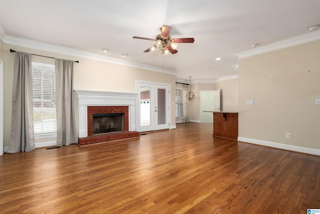 unfurnished living room with dark wood-type flooring, french doors, a brick fireplace, ceiling fan, and ornamental molding