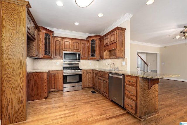 kitchen with kitchen peninsula, appliances with stainless steel finishes, tasteful backsplash, light stone counters, and light hardwood / wood-style flooring