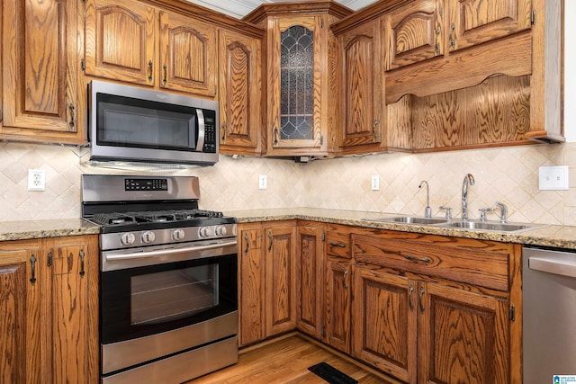 kitchen featuring sink, light stone counters, backsplash, appliances with stainless steel finishes, and light wood-type flooring