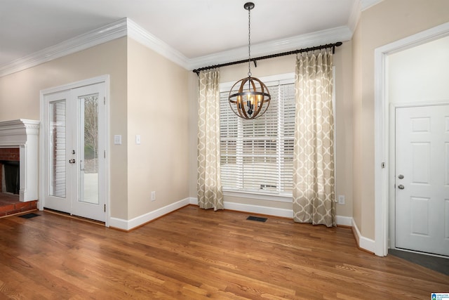 entrance foyer featuring wood-type flooring, a brick fireplace, crown molding, and a notable chandelier