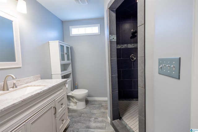 bathroom featuring a tile shower, vanity, and toilet