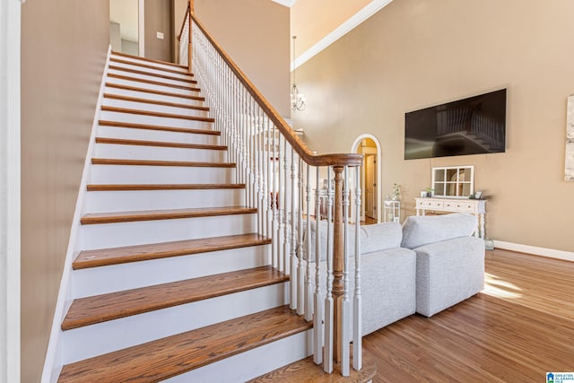 stairway with hardwood / wood-style floors, ornamental molding, and a towering ceiling