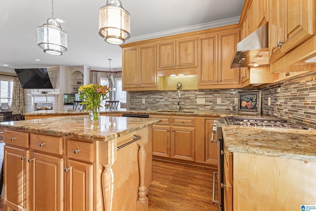 kitchen featuring wall chimney exhaust hood, high end stove, sink, decorative light fixtures, and a center island