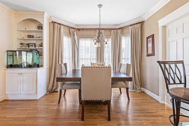 dining space featuring built in shelves, light hardwood / wood-style flooring, ornamental molding, and an inviting chandelier