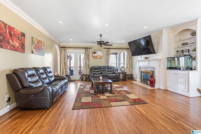 living room with french doors, built in shelves, ceiling fan, crown molding, and wood-type flooring