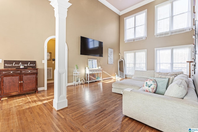 living room with hardwood / wood-style flooring, ornate columns, ornamental molding, and a towering ceiling