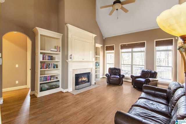 living room featuring built in shelves, ceiling fan, hardwood / wood-style floors, and a towering ceiling