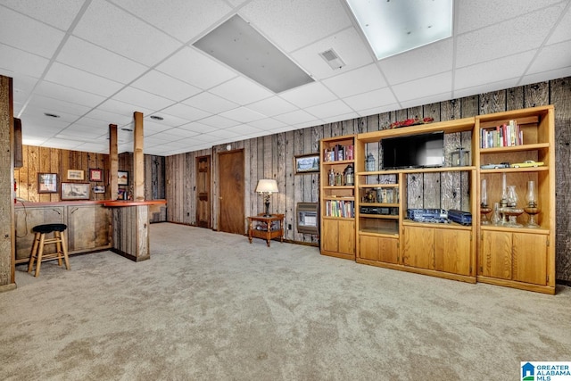 unfurnished living room featuring a drop ceiling, carpet, and indoor bar