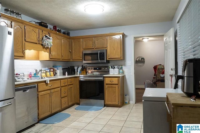 kitchen with backsplash, sink, light tile patterned floors, a textured ceiling, and appliances with stainless steel finishes