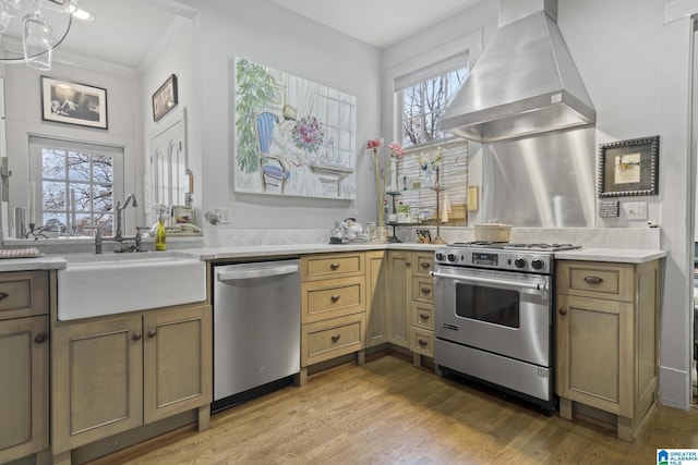 kitchen with wall chimney range hood, sink, light hardwood / wood-style flooring, appliances with stainless steel finishes, and a chandelier