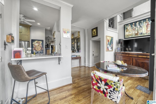 interior space featuring kitchen peninsula, a breakfast bar, ceiling fan, crown molding, and hardwood / wood-style flooring