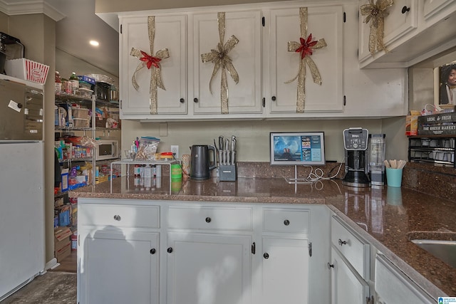 kitchen featuring dark stone countertops, white cabinets, and fridge