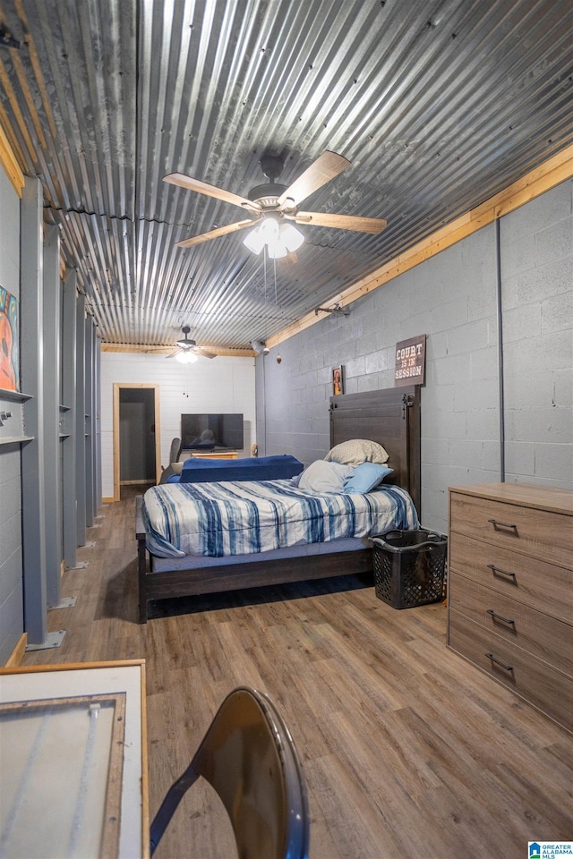 bedroom with ceiling fan, wood finished floors, and concrete block wall