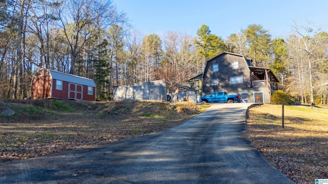 view of home's exterior featuring an outbuilding, a shed, a gambrel roof, and driveway