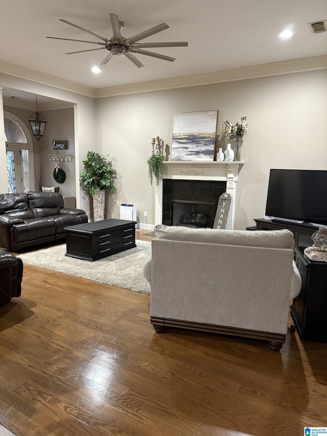 living room featuring dark hardwood / wood-style floors, ceiling fan, crown molding, and a tile fireplace