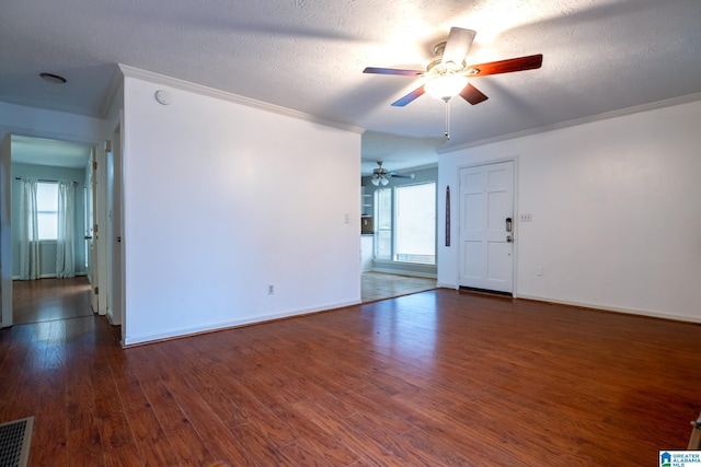 empty room with a textured ceiling, crown molding, and dark wood-type flooring