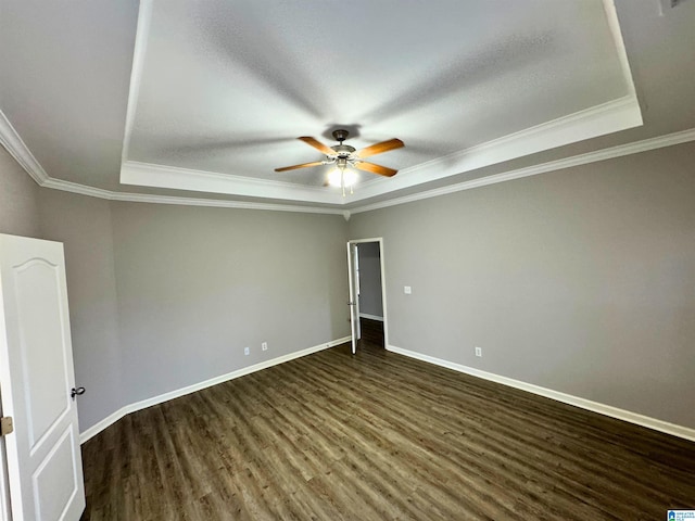 empty room with dark hardwood / wood-style floors, ceiling fan, ornamental molding, and a tray ceiling