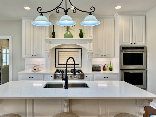 kitchen featuring hanging light fixtures, white cabinetry, a center island with sink, and stainless steel double oven