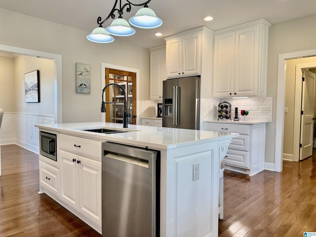 kitchen with white cabinets, sink, stainless steel appliances, and an island with sink