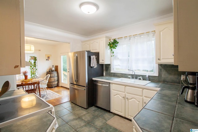 kitchen with backsplash, sink, crown molding, tile counters, and stainless steel appliances