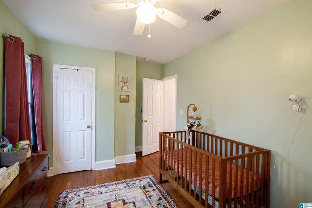 bedroom featuring a crib, ceiling fan, and dark wood-type flooring