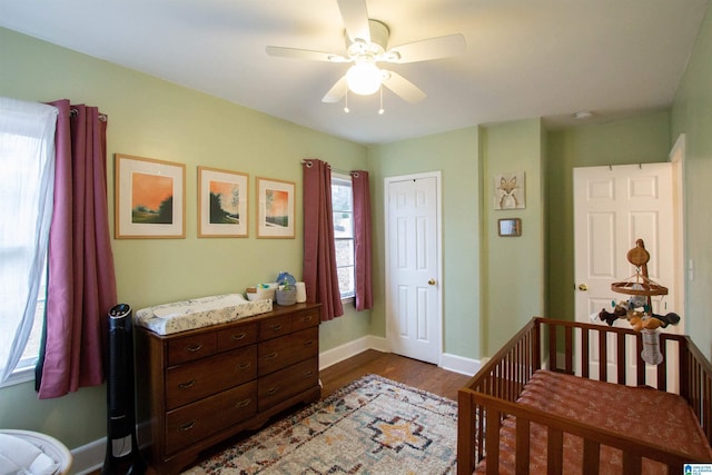 bedroom featuring a closet, ceiling fan, dark hardwood / wood-style flooring, and a nursery area