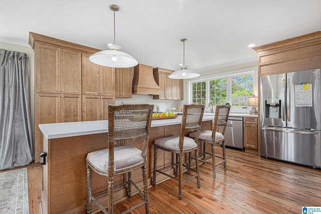 kitchen featuring custom range hood, stainless steel appliances, crown molding, decorative light fixtures, and hardwood / wood-style flooring