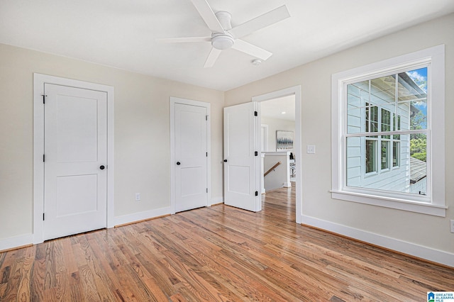 unfurnished bedroom with ceiling fan, hardwood / wood-style floors, and two closets