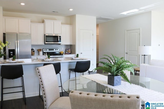 kitchen with dark hardwood / wood-style flooring, backsplash, stainless steel appliances, white cabinetry, and a breakfast bar area