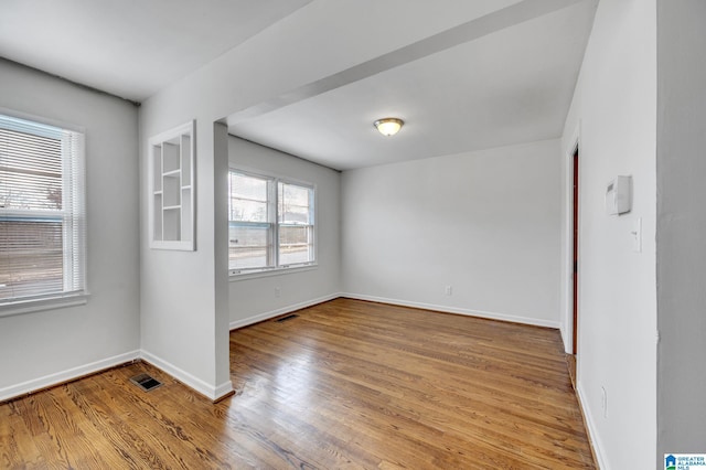 empty room featuring built in shelves and hardwood / wood-style flooring