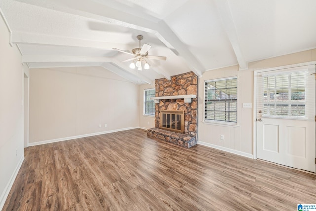 unfurnished living room featuring hardwood / wood-style flooring, vaulted ceiling with beams, ceiling fan, and a stone fireplace