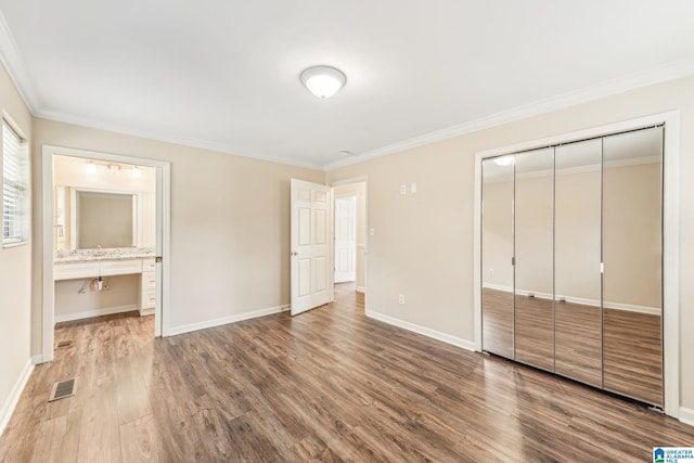 unfurnished bedroom featuring crown molding, built in desk, hardwood / wood-style floors, connected bathroom, and a closet