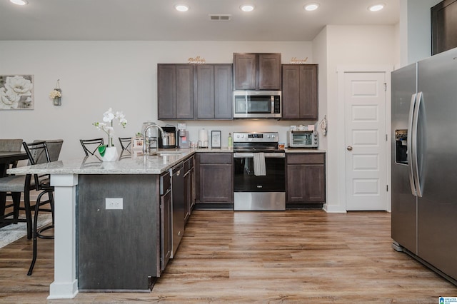 kitchen with kitchen peninsula, stainless steel appliances, sink, light hardwood / wood-style floors, and a breakfast bar area