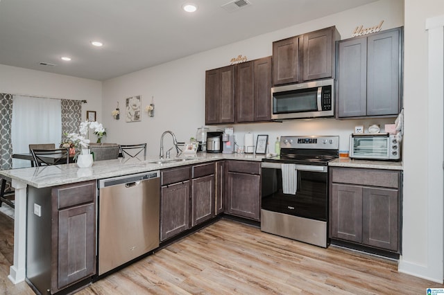 kitchen with light stone countertops, sink, kitchen peninsula, appliances with stainless steel finishes, and light wood-type flooring