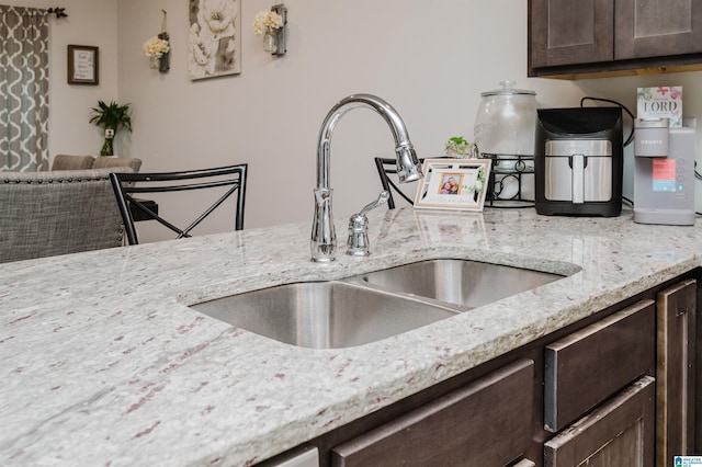 kitchen featuring light stone countertops, dark brown cabinets, and sink