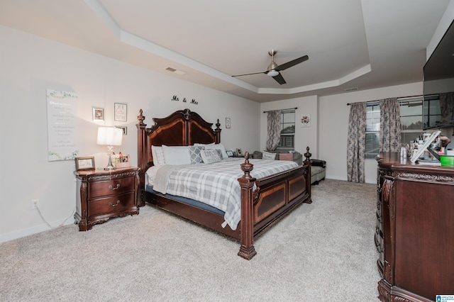 carpeted bedroom with ceiling fan and a tray ceiling