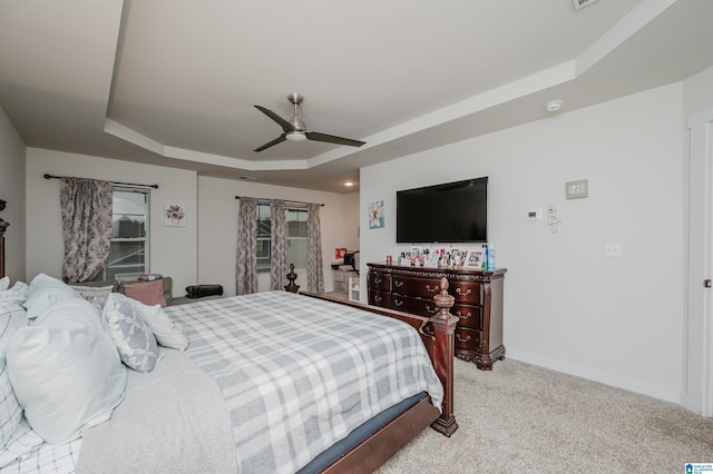 bedroom with ceiling fan, light colored carpet, and a tray ceiling