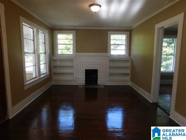 unfurnished living room with built in features, a brick fireplace, dark wood-type flooring, and crown molding