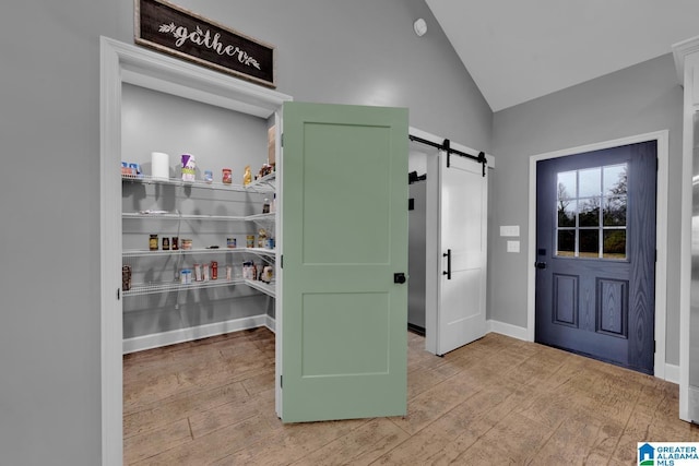 entryway with light wood-type flooring, a barn door, and vaulted ceiling