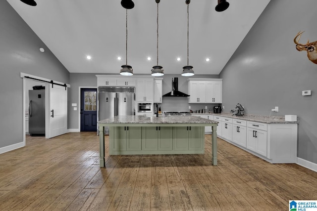 kitchen with white cabinets, wall chimney exhaust hood, a barn door, decorative light fixtures, and stainless steel refrigerator