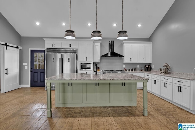 kitchen with wall chimney exhaust hood, hanging light fixtures, stainless steel appliances, a barn door, and a breakfast bar