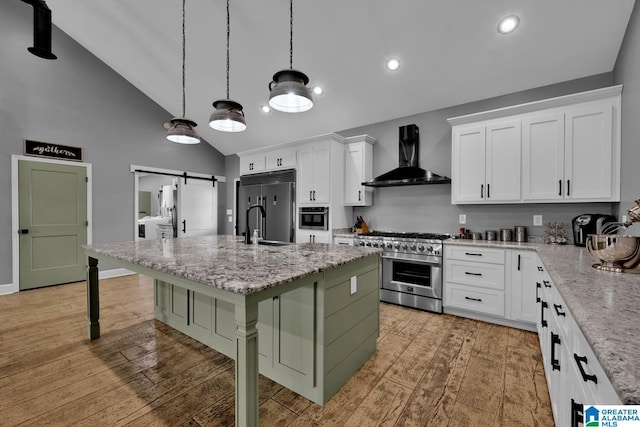 kitchen with a center island with sink, white cabinets, wall chimney range hood, a barn door, and a breakfast bar area