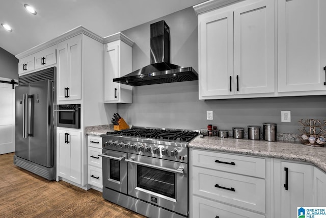 kitchen featuring light stone countertops, wall chimney range hood, hardwood / wood-style floors, high quality appliances, and white cabinets